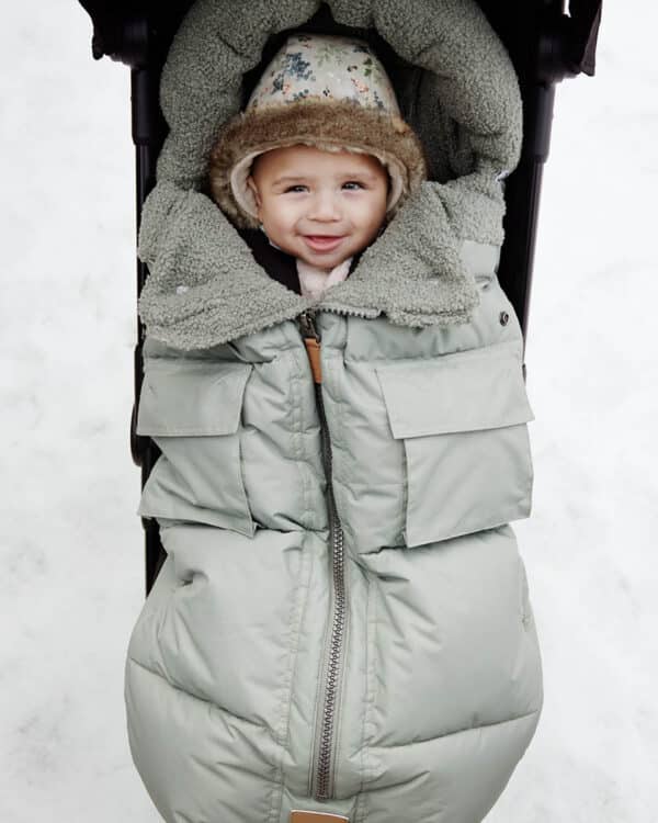 Bébé en poussette dans la neige avec chancelière Hazy Jade