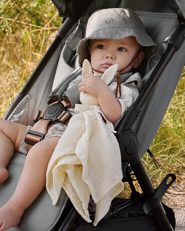 Bébé assis dans la poussette compacte Elodie MONDO Hazy Jade tenant son doudou lange Otis