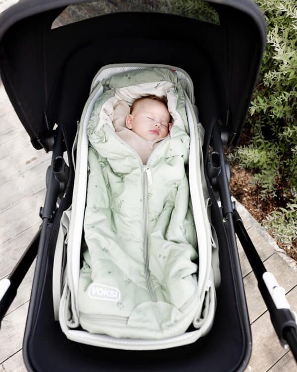 Bébé endormi dans le Voksi Carry Me vert brume, installé dans une poussette avec canopy.