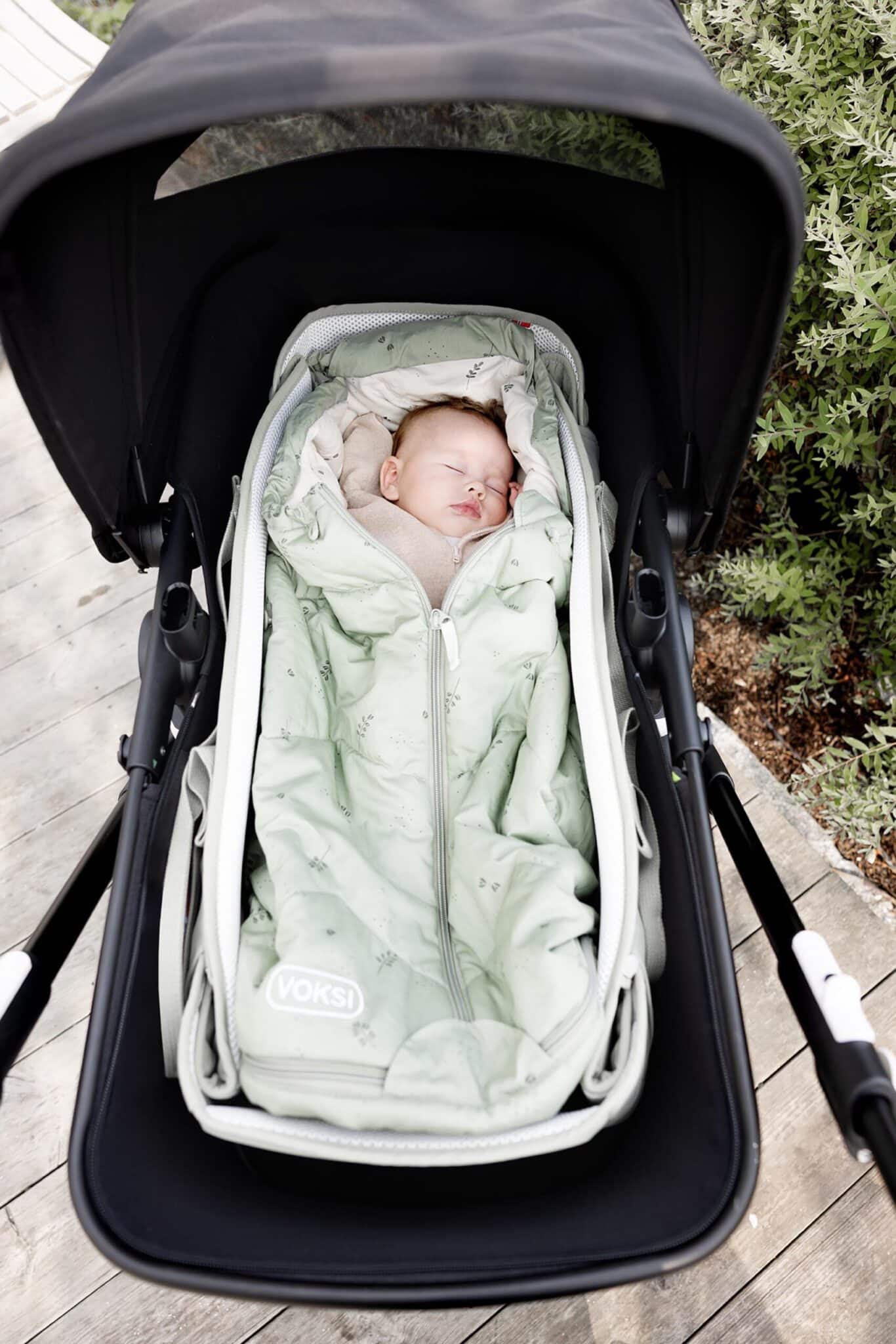 Bébé endormi dans le Voksi Carry Me vert brume, installé dans une poussette avec canopy.