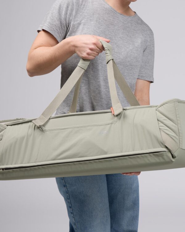 Voksi Carry Me vert sauge portée à la main, couffin de transport bébé avec anses et fermeture zippée.
