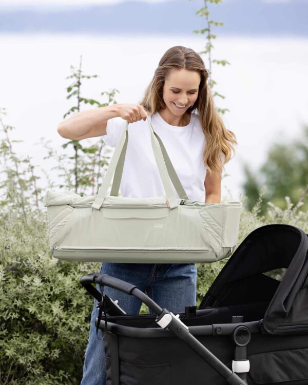 Maman place la Voksi Carry Me Misty Green sur une poussette, couffin nomade portable pour bébé.