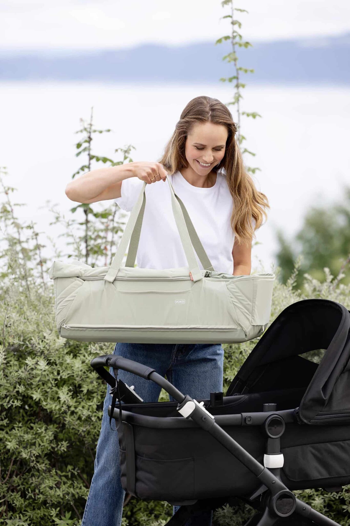 Maman place la Voksi Carry Me Misty Green sur une poussette, couffin nomade portable pour bébé.