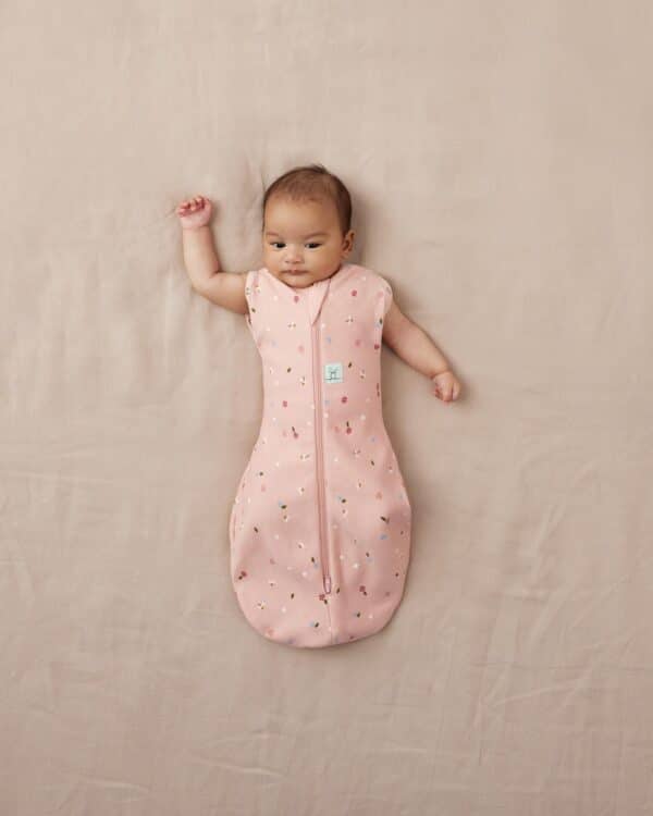 Bébé allongé portant le cocon d’emmaillotage ergoPouch Cocoon Daisies rose poudré fleuri, vue du dessus