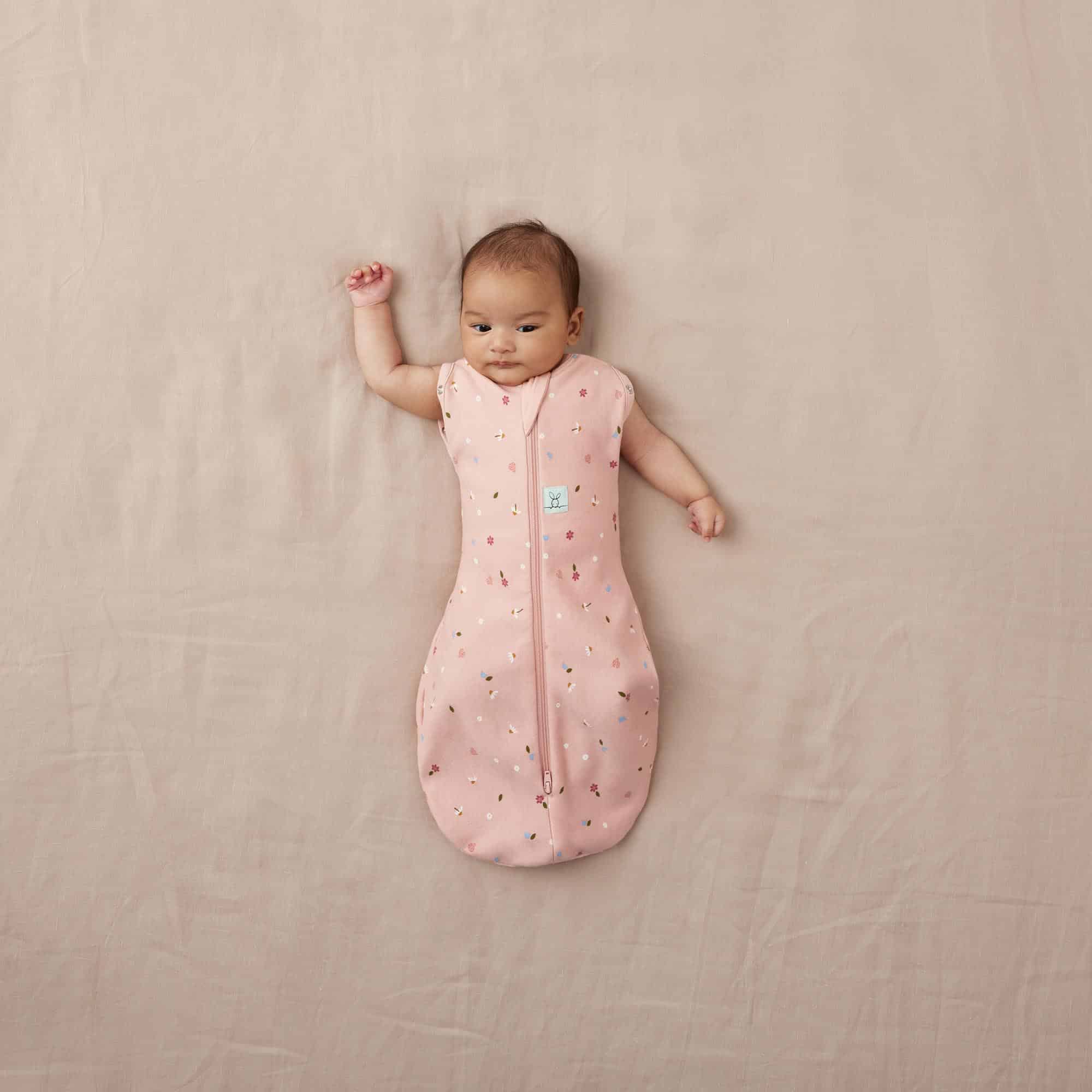 Bébé allongé portant le cocon d’emmaillotage ergoPouch Cocoon Daisies rose poudré fleuri, vue du dessus