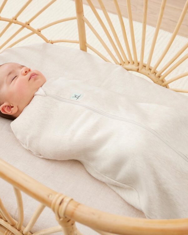 Bébé endormi portant le cocon d’emmaillotage ergoPouch Cocoon Oatmeal Marle beige chiné, gros plan dans un berceau