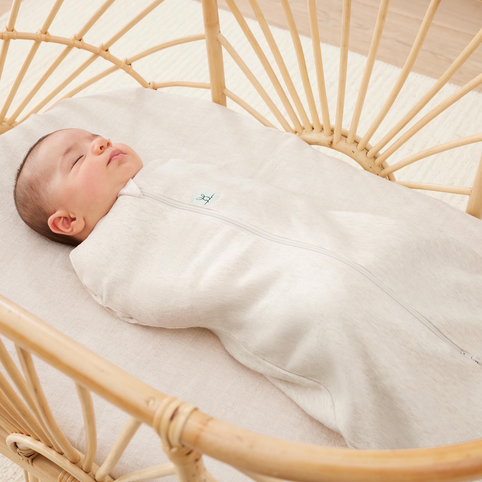 Bébé endormi portant le cocon d’emmaillotage ergoPouch Cocoon Oatmeal Marle beige chiné, gros plan dans un berceau