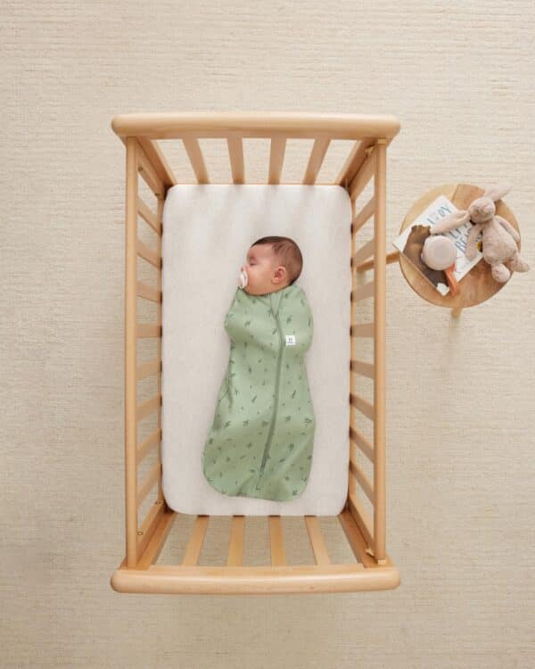 Bébé dans un lit en bois portant le cocon d’emmaillotage ergoPouch Cocoon Willow vert feuillage, vue du dessus