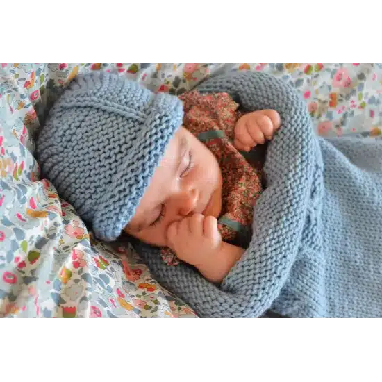 Bébé endormi dans un cocon de naissance en laine mérinos bleu layette, style emmaillotage