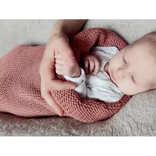 Bébé endormi dans un cocon de naissance en laine mérinos terracotta rosé, emmaillotage doux