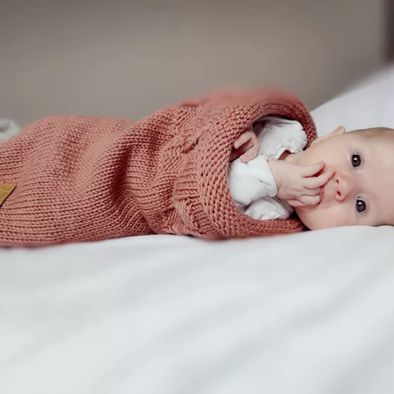 Bébé dans un cocon de naissance en laine mérinos terracotta rosé, mains accessibles pour l’auto-apaisement