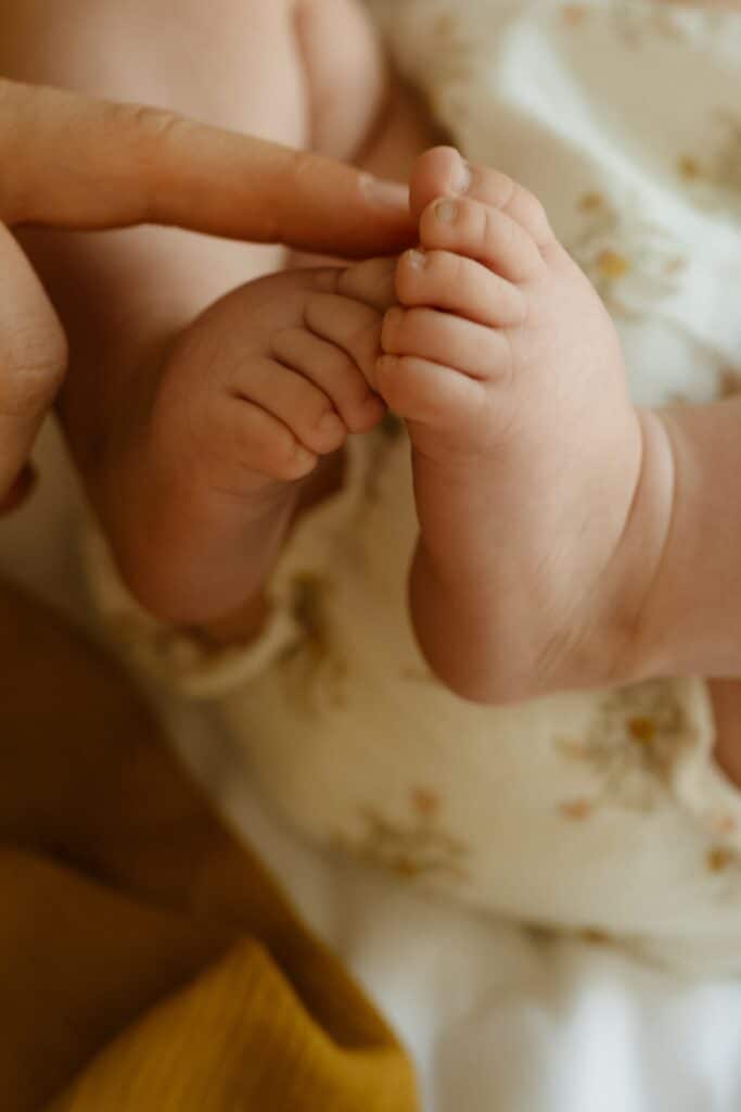 Main d’un parent touchant les petits pieds d’un bébé, symbole de douceur et de lien autour de la naissance